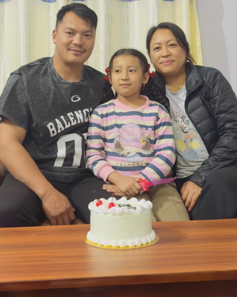 黒い服を着た夫婦とピンク色の服の子供がケーキを前に笑顔で座っているイメージ