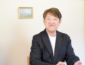 黒いジャケットを着た男性が座って微笑む様子